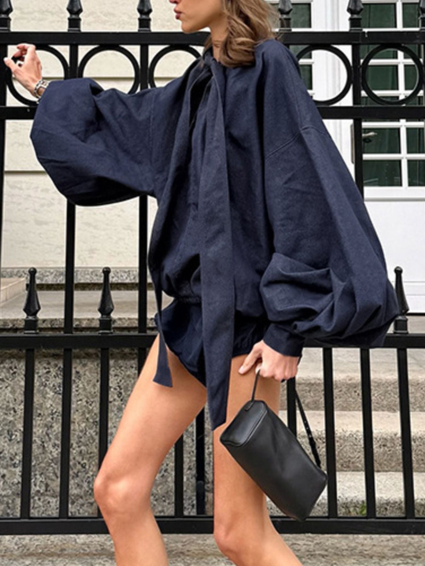 model wearing a navy blue top with balloon sleeves  and short shorts walking outdoors.